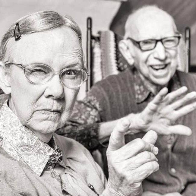 Toned image of angry old couple sitting in living room woman pointing